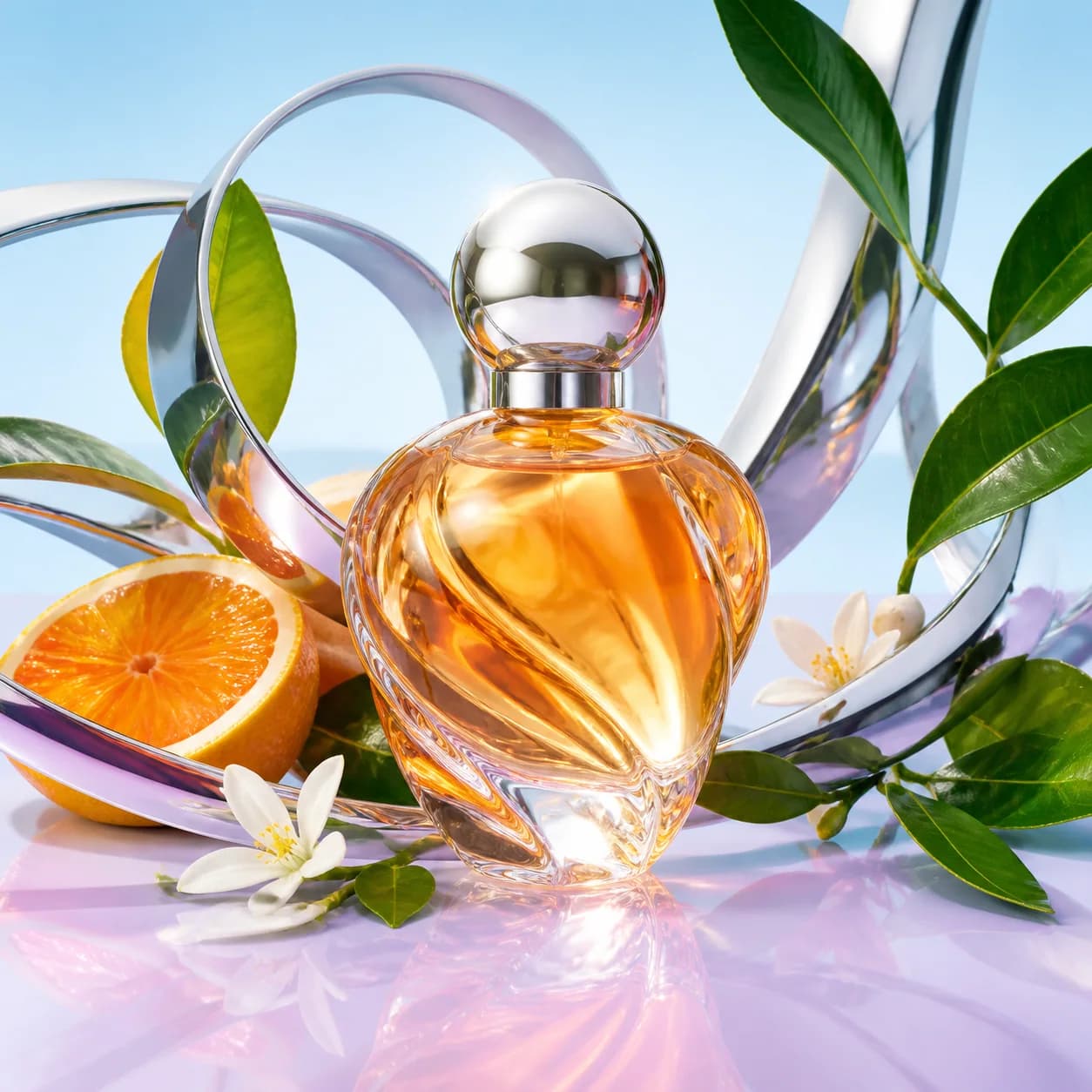 An unlabeled citrus glass perfume bottle framed by chrome ribbons and green leaves