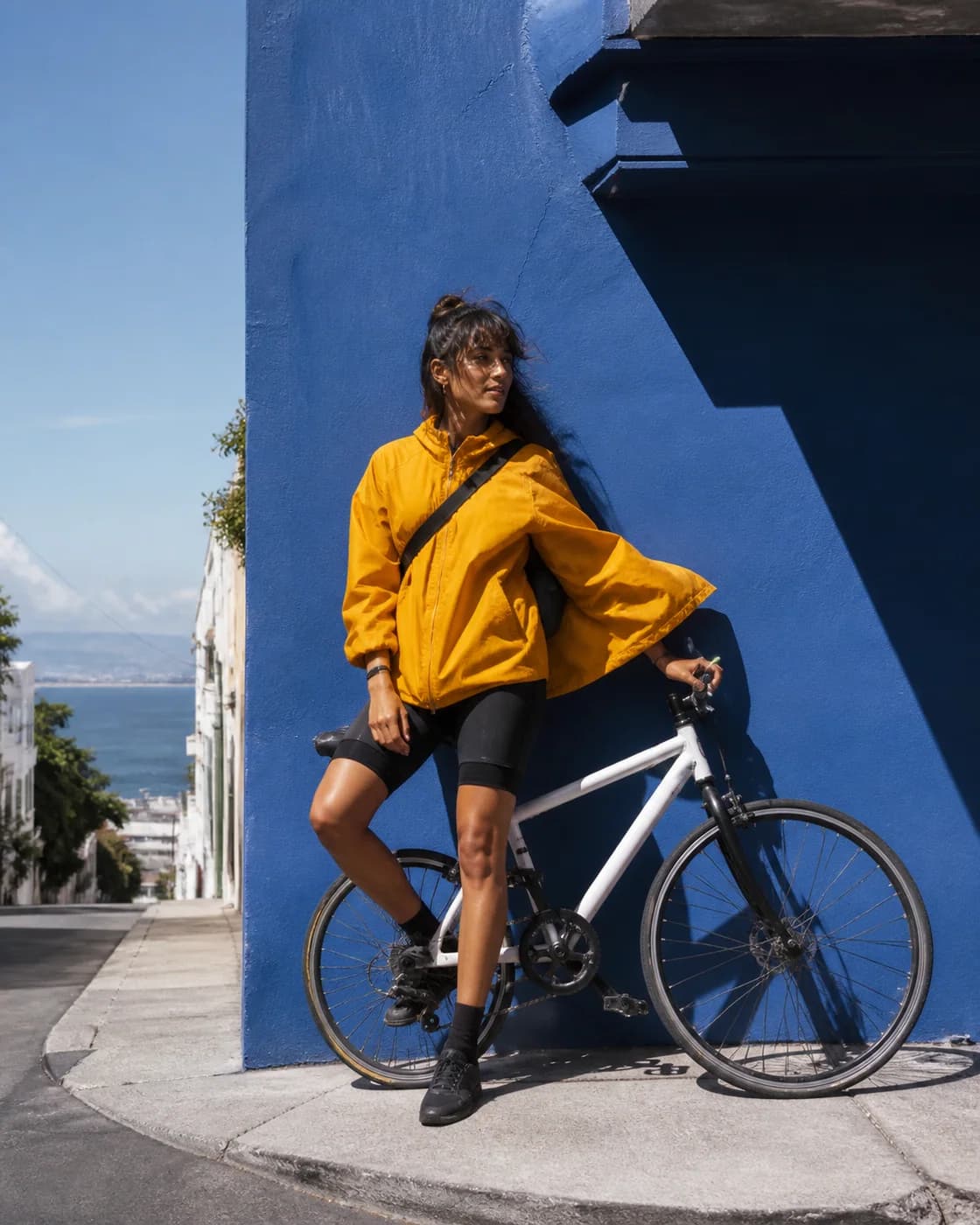 A fictional adult bicycle messenger in a saffron jacket beside a cobalt wall